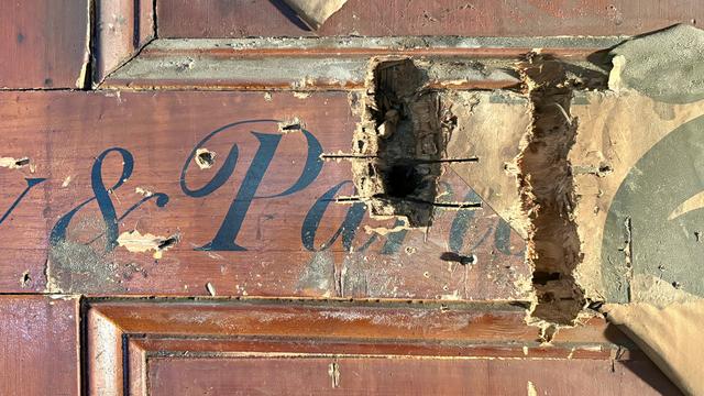 Detail of the wood-panelled wall, and the signwritten lettering on it that can be read as '& Par___' with the latter part obscured by the bill poster.