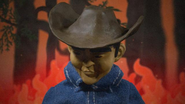 A claymation cowboy stands in front of a stop-motion forest wildfire