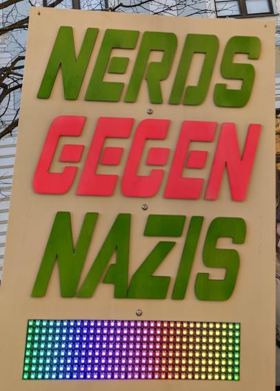 Demoschild mit dem Text "Nerds gegen Nazis" und regenbogenfarbener LED-Anzeige.