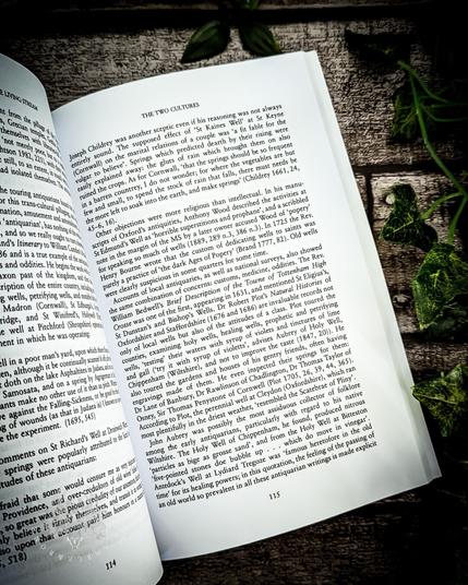 A page from The Living Stream: Holy Wells in Historical Context, showing the section titled "The Two Cultures." This page discusses Joseph Childrey's skepticism regarding holy wells, specifically the belief surrounding St. Keyne's Well in Cornwall. It details his thoughts on the spring's purported magical properties and its connection to superstitions. The text also touches on early antiquarians' interest in these wells, including references to antiquarians such as Anthony Aubrey and the customs surrounding holy wells. The page is placed on a rustic background with green ivy leaves.