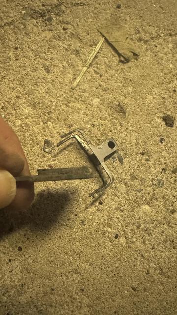 Eine Nahaufnahme einer Hand, die ein kleines Metallteil mit einem gegabelten Design hält und auf einer strukturierten Oberfläche ruht. In der Nähe sind kleinere Trümmer wie Blätter und kleine Stöcke sichtbar.
Das Metallteil ist ein Bremsbelag meiner Scheibenbremse.