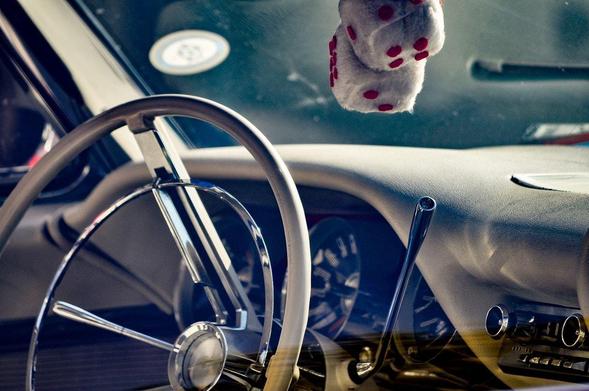 This image depicts the interior of a vintage car. You can see a classic steering wheel and dashboard, along with fuzzy dice hanging from the rearview mirror. The overall vibe is retro, and elements like the dashboard and steering wheel suggest an older model vehicle.