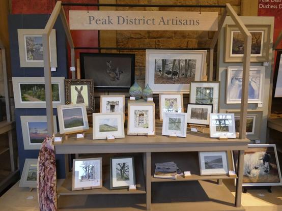 A "market stall" style display with lots of framed artworks. The sign at the top reads Peak District Artisans. Two vertical units at each side have artwork hunf on them