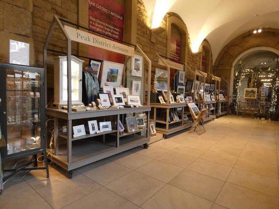 A long shot of four market stall styled display units holding framed artworks and display cabinets holding jewellery