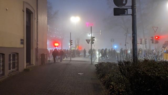 Eine Menschenmenge watet von links durch den Nebel. Es sind einige Lichter von Ampeln zu sehen.