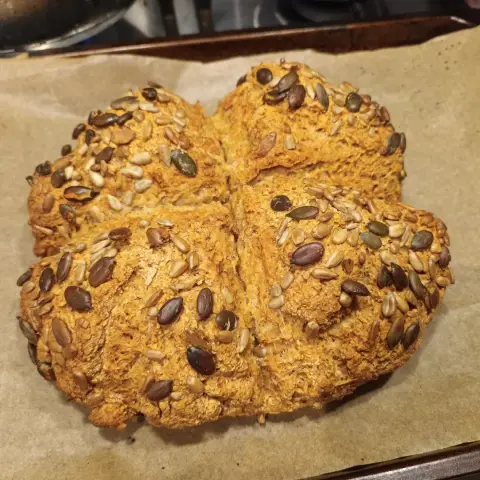 A loaf of soda bread, nicely browned on top and sprinkled with sunflower and pumpkin seeds.