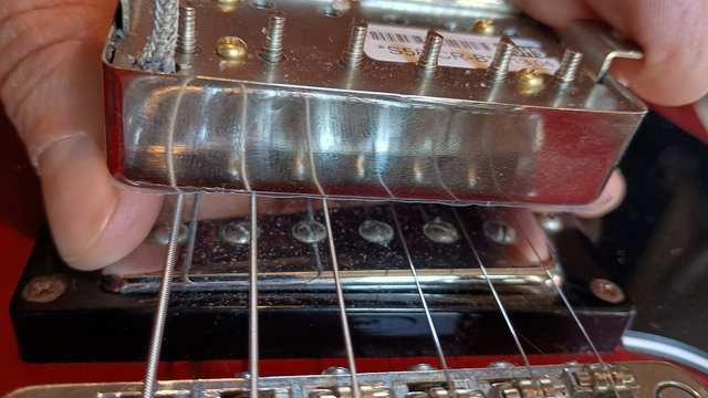 Close up of the bridge pickup and strings of a red Epiphone Dot 335. My hand is holding another shiny new pickup above the strings.
The new pickup's wire is connected to an instrument cable with alligator clip leads.
I can switch back and forth between the new pickup and the one in the guitar by switching the instrument cable from the guitar with the one from the new pickup, going into the pedalboard.