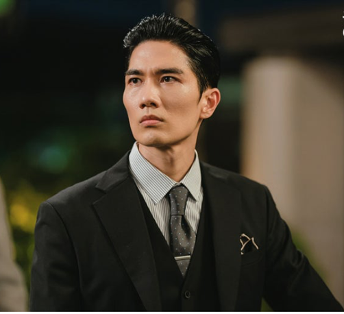 Handsome Korean actor with cheekbones for miles wearing a suit and serious or slightly alarmed expression.