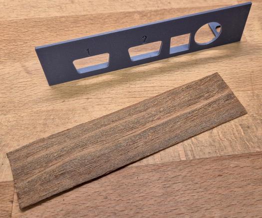 A 3d-printed C64 side bracket with a piece of veneer beside it.