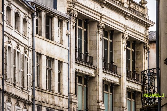 A close-up of historic stone architecture in La Rochelle showcasing intricate columns, iron balconies, and shuttered windows. The inscription "Nouvelles Galeries du Petit Saint-Thomas" is visible, evoking a sense of classic French elegance.