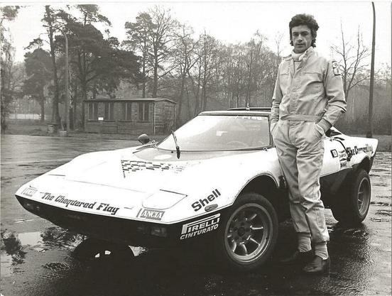 A black and white photo of racing driver Tom Pryce standing nexy to a Lancia Stratos rally car.