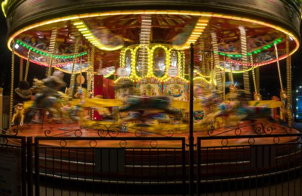 Photo of a carousel, brightly lit up at night. The horses and other moving elements of the ride are blurred with motion.