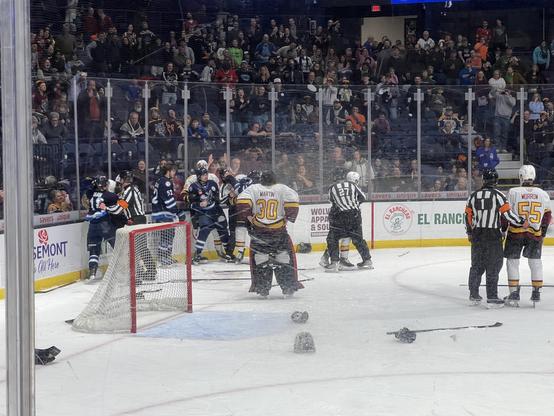 A hockey brawl behind the net. Sticks and gloves are strewn about on the ice