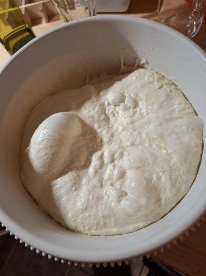 Valkoisessa taikinakulhossa focacciataikina, jonka pinnalla ilmakuplia