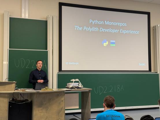 Photo of a person on stage in front of a screen with the text Python Monorepos The Python Developer Experience.