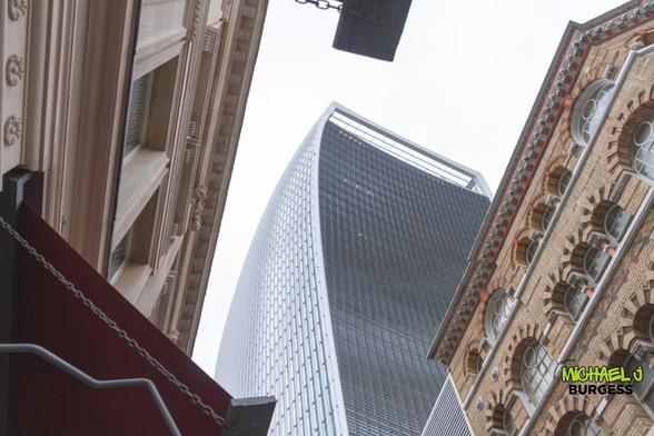 This is a low-angle perspective of London's Walkie-Talkie building (20 Fenchurch Street), framed by historic brick and stone architecture. The juxtaposition of the city's modern skyscrapers and rich architectural heritage is striking.