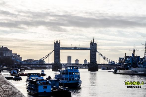 A stunning view of London's Tower Bridge at dusk, framed by boats navigating the River Thames. The sky is painted with soft hues, casting a serene atmosphere over the historic landmark and surrounding cityscape.
