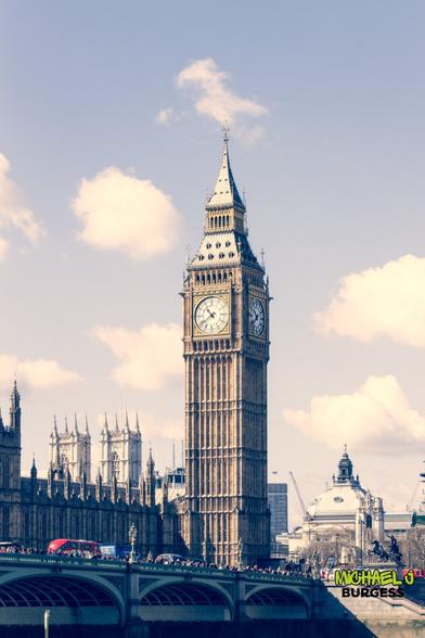 A classic view of Big Ben and the Houses of Parliament bathed in soft light with a vintage aesthetic. The iconic London red bus crosses Westminster Bridge, adding a touch of movement to this timeless scene. Puffy clouds in the background frame the historic landmark beautifully.