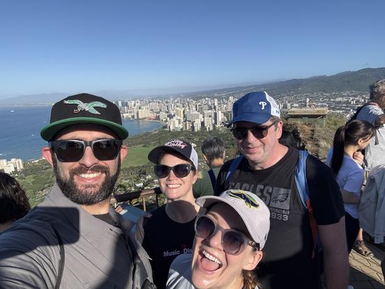 Group photo in front at the top of Diamondhead overlook, with Honolulu cityscape in the background.