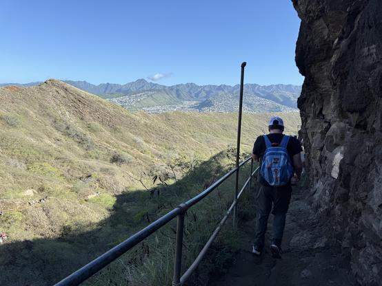 Walking along the Diamondhead hiking trail carved out of the side of a mountain with lush mountainous landscape in the background.