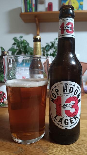 Auf einem Tisch steht ein Glsd mit hellbraunen klarem Bier gefüllt.
Daneben die passende Bierflasche mit Etikett auf dem steht:

Hop House 13 Lager