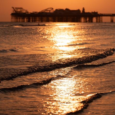 A stream of sunlight turning the surface of the water/waves into gold, with the out of focus pier behind