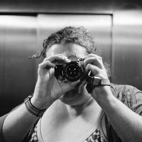 A black and white picture of gemma taking a picture of herself, with an olympus om1 camera