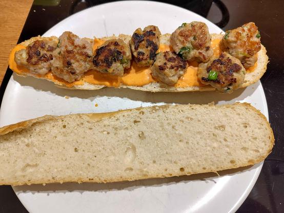 Biały talerz, na nim półbagietka ze sriracha mayo i pulpecikami wieprzowymi