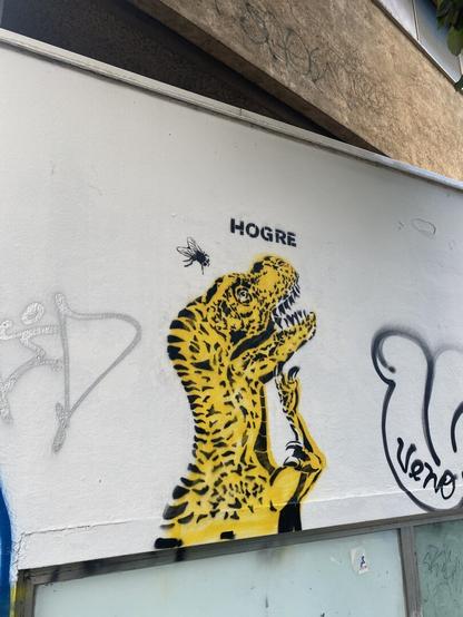 A yellow dinosaur with a fly, stencil on wall.