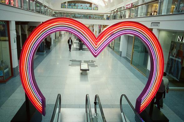 a neon heart arch around the bottom of an escalator inside a mall
