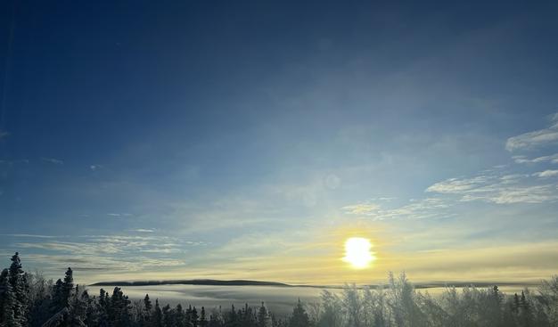 Yellow Sun rising over a fog filled Goldstream Valley with Ester Dome peaking out under a blue sky.