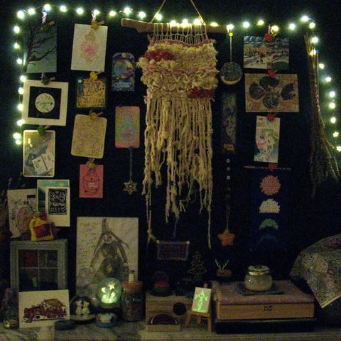 Dark photo taken at nighttime of an altar with shining fairy lights, an LED tea light covered with felt crystal ball "hat", and a glow-in-the-dark sigil painted on a tiny canvas.