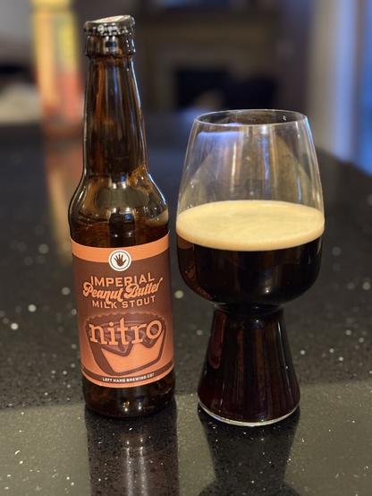 A brown 12 ounce bottle with an orange and brown label shows a stylized peanut butter cup with a bite the shape of a crown. A stout glass full of beer is to the right