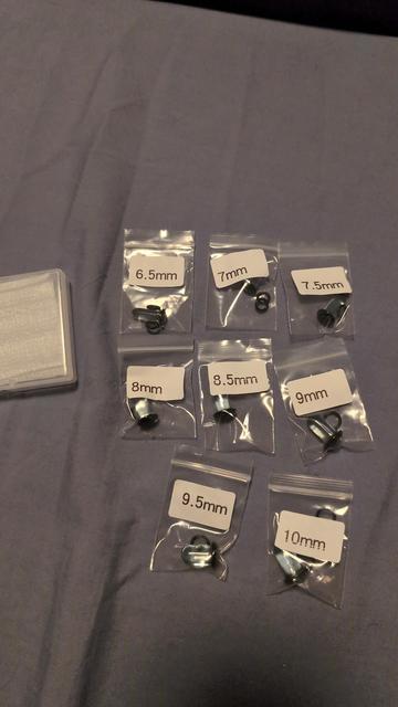 A bluish-grey background that is my bedsheet. On it is 8 small baggies, with white labels that say (from top left) 6.5mm, 7mm, all the way up like that to 10mm. I side the bag are glass plugs with a small black rubber band.