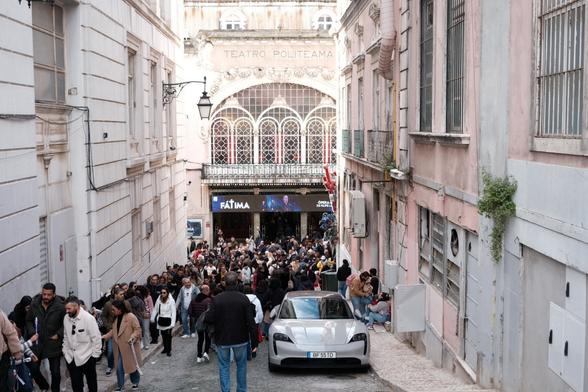 Picture of the Politeama Theatre and a huge crowd in front of it. A single car, a grey Porsche, is parked on the street.