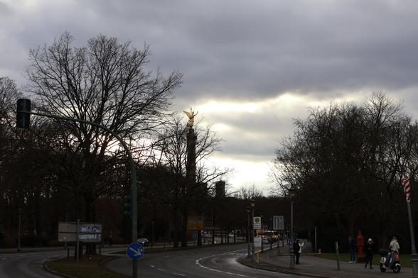 Siegessäule Berlin in der Ferne bei grauem Himmel.
Baumsilhouetten verdecken sie