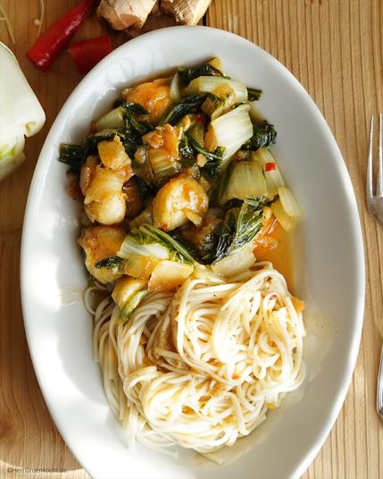 Heller Holzuntergrund. Darauf ein weißer ovaler Teller. Darin: »Geschmorter Pak Choi mit Bananen, Ingwer, Peperoni, Zwiebeln, Kreuzkümmel und mit Ramen-Nudeln«