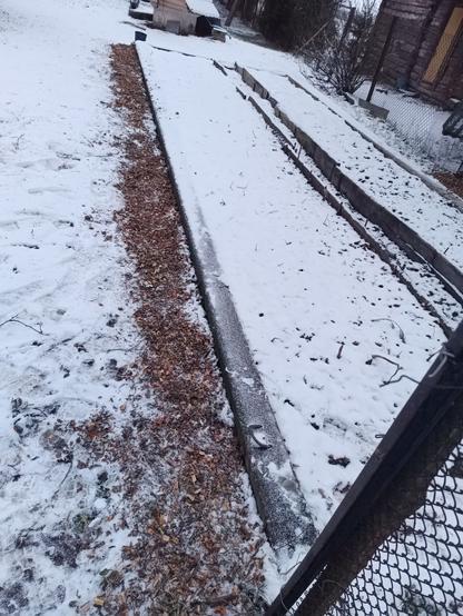 A garden plot covered in snow. Some fresh branch mulch is spread alongside it, wide enough to walk on.