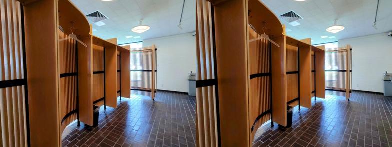 Stereoscopic, side-by-side view. Looking at the inside of a divider in the lobby of the Mt. Angel Library. It is made of thin, vertical blonde wood slats, about one inch thick, separated by similar-sized gaps. It has an undulating shape, curving inward at the ends. (We are looking at the concave side.) The slats are supported by a black steel frame. On the underside of the "lid" of the structure are some coat hooks.