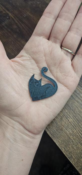 Photo of a cute little flat cat pendant I 3D printed in the same sparkly blue
