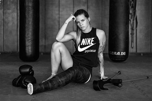 Female kickboxer sitting on the ground of the trainings room with boxing gloves and crutches besides her. She has a full legcast on her left leg.