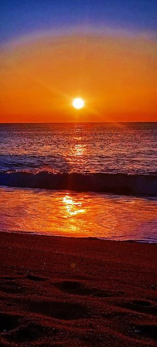 Salida del Sol en el pueblo costero de Malgrat de Mar. Luz naranja sobre un mar azulado.
