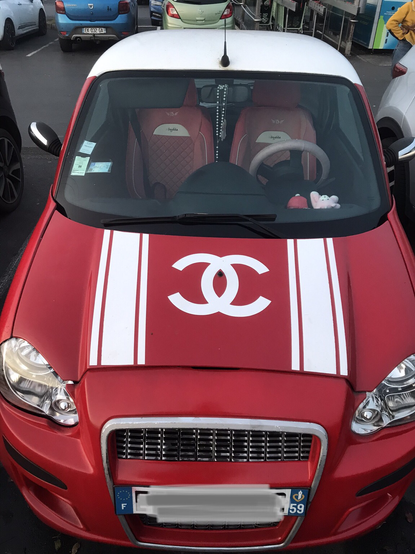 Photographie d'une voiture rouge sur laquelle le.a propriétaire à coller un autocollant du logo Chanel