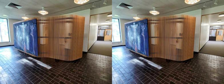Stereoscopic, side-by-side view. Looking at the outside of a divider in the lobby of the Mt. Angel Library. It is made of thin, vertical blonde wood slats, about one inch thick, separated by similar-sized gaps. It has an undulating shape, curving towards the wall at the ends. (We are looking at the convex side.) It is just tall enough to hide the restroom doors behind it, and is elevated a couple inches above the floor. There is a modern (well, late 20th century, anyway) painting of the crucifixion along one flat part.