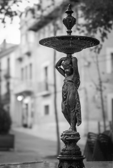 Black and white photography in which you can see a fountain statue that It carries a plate over its shoulders.