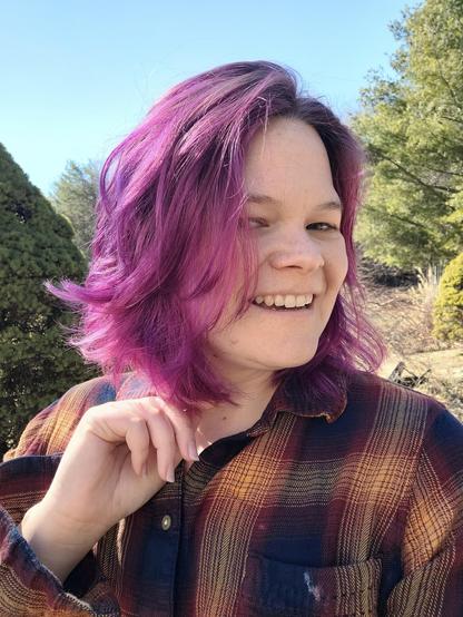 A woman looks into the camera smiling. Her bright hair seeming to glow in sunlight.