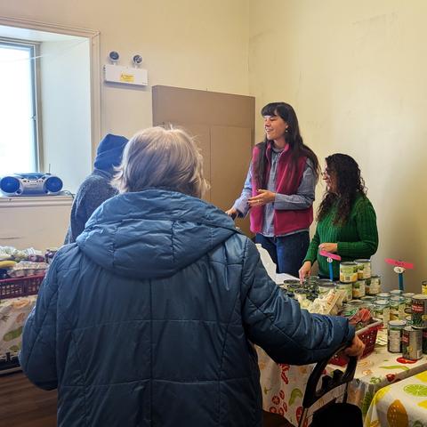 Plusieurs personnes se tiennent de part et d'autre d'une table où l'on retrouve des denrées alimentaires.