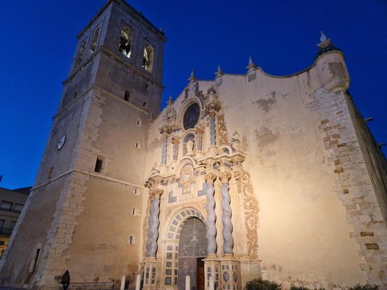 Façana de l'església arxiprestal de Vinaròs il·luminada i amb el cel vlau fosc de fons.