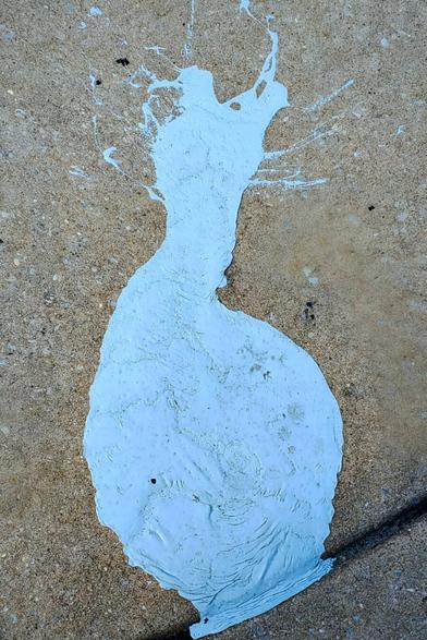 Blue paint spilled on a sidewalk. It looks somewhat like the outline of a woman's dress.