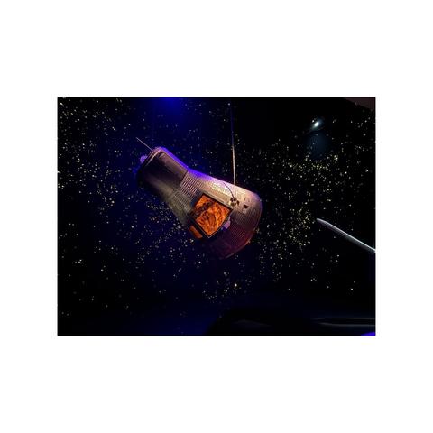 a space capsule with an illuminated window floats through a dark diorama